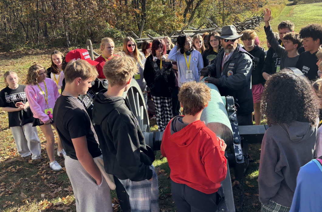A group of students around a cannon and listening to a park ranger. 