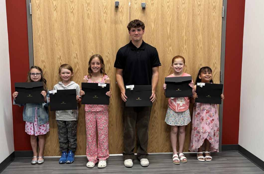 Six students holding certificates stand in front of double wooden doors. 