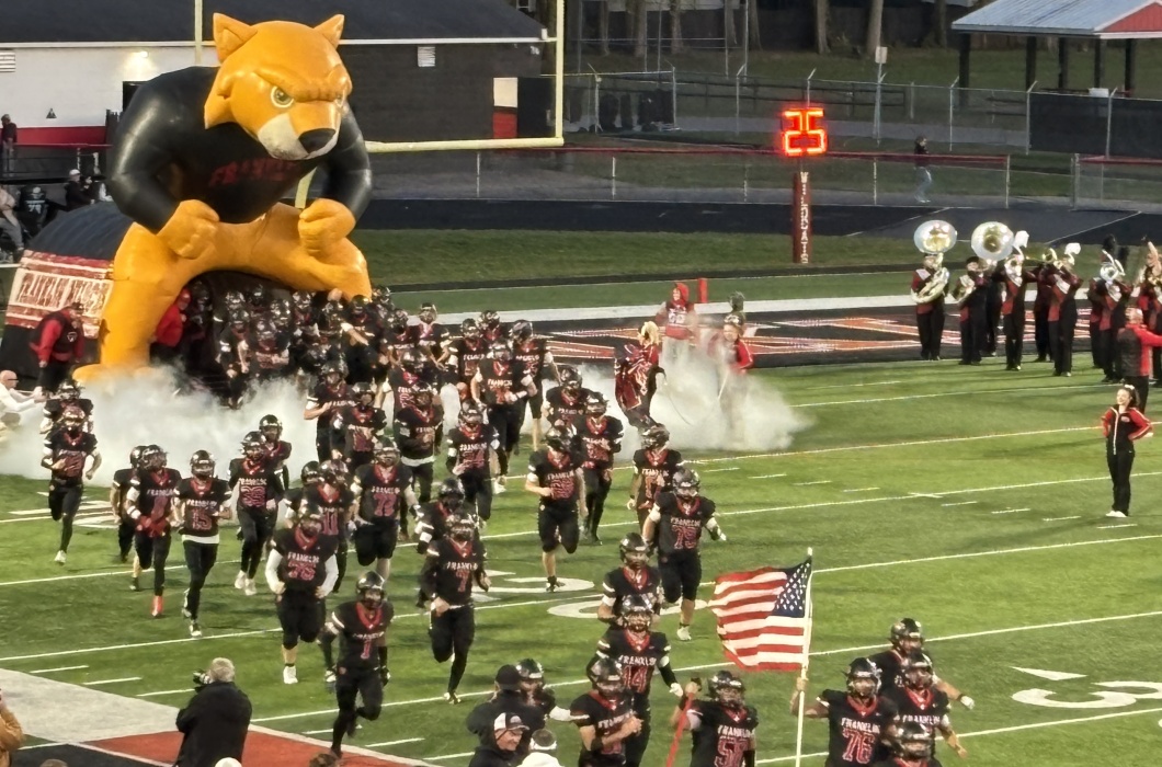 Football players run onto the field while the band plays. 